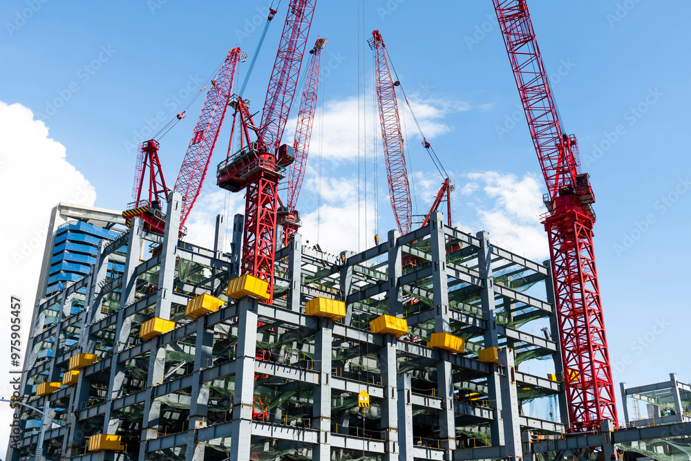 Low-angle view of cranes and steel structures of building construction with a blue sky background in Taiwan.