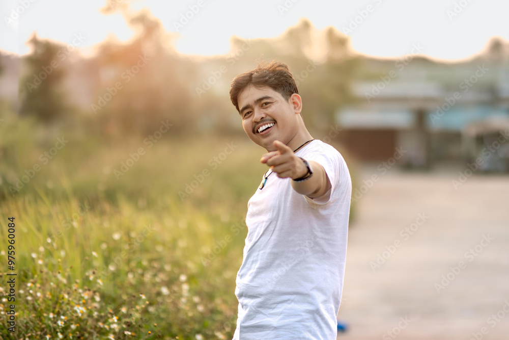 Fototapeta premium a man standing and smiling. the man points at the camera in the sunny afternoon.