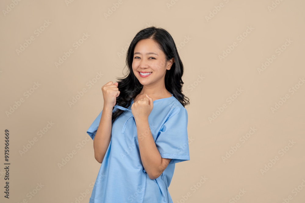 Happy young Asian female patient wearing a patient gown from an accident on a cream background Happy young Asian female patient wearing a patient gown from an accident on a cream background