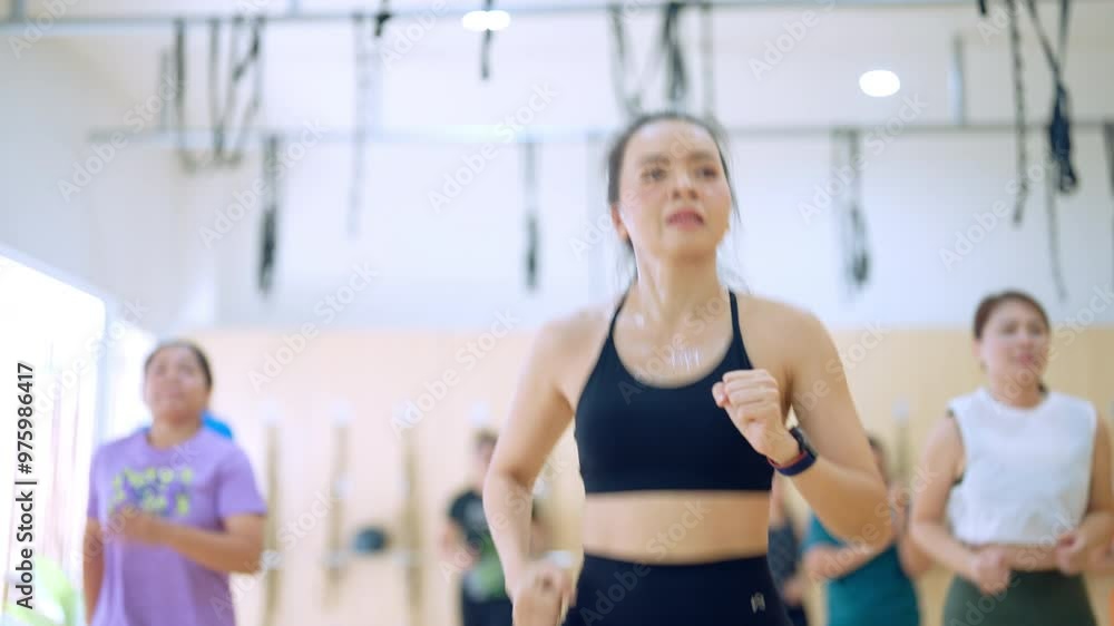 A woman is running in a gym with other people. Scene is energetic and active A woman is running in a gym with other people. Scene is energetic and active