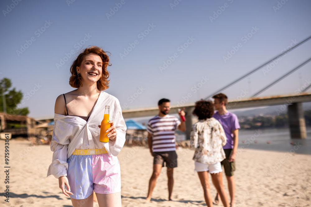 Young ginger girl is drinking orange juice at the beach while her friends are hanging out behind her. Young ginger girl is drinking orange juice at the beach while her friends are hanging out behind her.