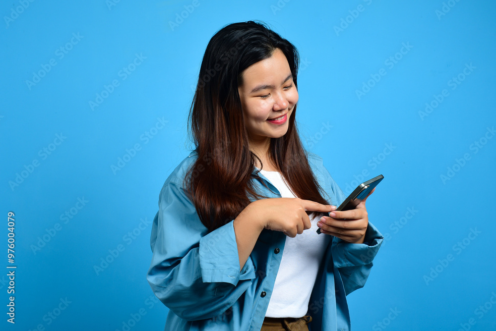 Young happy asian woman online shoping, fingers pointing while holding a cell phone in the other hand, Standing and pointing happily, light blue back ground. Copy space Young happy asian woman online shoping, fingers pointing while holding a cell phone in the other hand, Standing and pointing happily, light blue back ground. Copy space