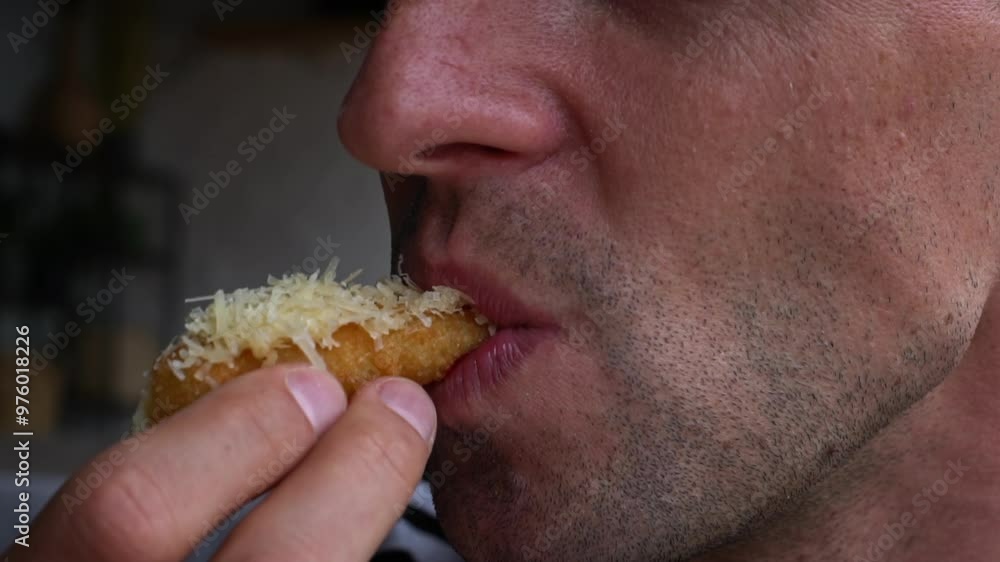 Close-up shot of a man eating a fried cheesy snack with ketchup. The shot is from the side, and the man's mouth is in focus. Close-up shot of a man eating a fried cheesy snack with ketchup. The shot is from the side, and the man's mouth is in focus.