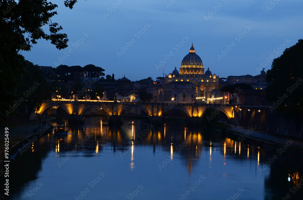 Obraz premium Castel Sant'Angelo in Rome, beautifully illuminated and reflecting on the calm river. The dark blue sky contrasts with the warm lights of the castle.