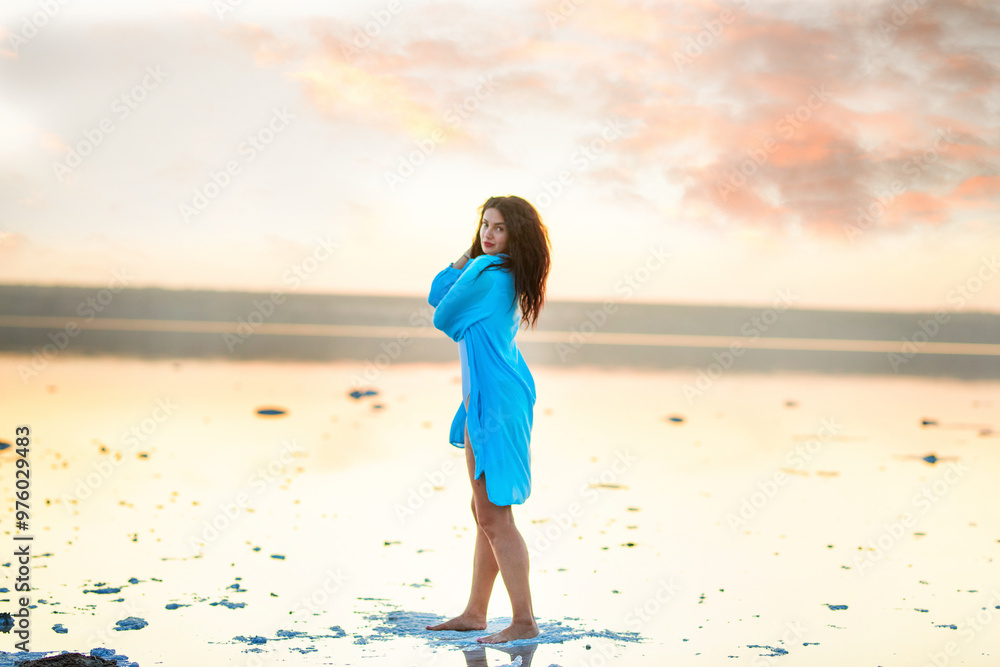 a brunette girl with curls walks relaxed in the water of a salt lake at sunset. happy calm woman with a cute smile in a loose blue shirt. a brunette girl with curls walks relaxed in the water of a salt lake at sunset. happy calm woman with a cute smile in a loose blue shirt.