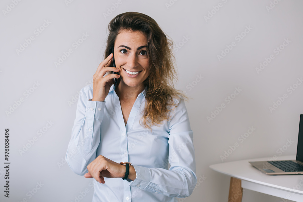 Smiling young woman with wristwatch talking on phone and looking at camera Smiling young woman with wristwatch talking on phone and looking at camera
