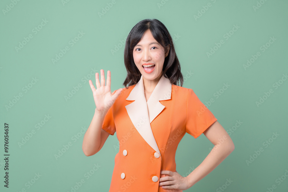 Happy woman waving in orange outfit against green background, expressing joy and friendliness Happy woman waving in orange outfit against green background, expressing joy and friendliness