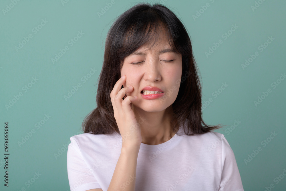 A woman is experiencing dental pain, holding her cheek with pained expression against green background. This image captures discomfort associated with toothache A woman is experiencing dental pain, holding her cheek with pained expression against green background. This image captures discomfort associated with toothache