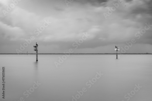 Picnic Island Park Tampa Florida 2 channel markers in calm water, with a cloudy sky creating dramatic ambiance. The horizon is barely visible, adding to the serene and minimalist composition. photo