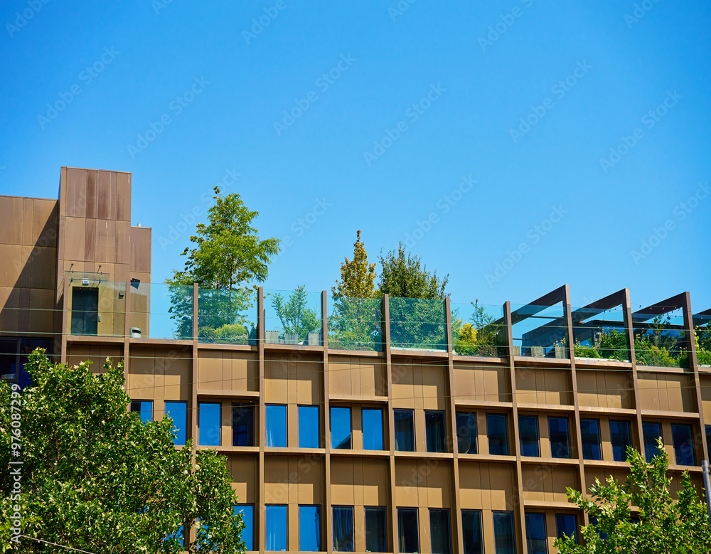 Contemporary building with rooftop garden. Green space in urban architecture under clear blue sky.