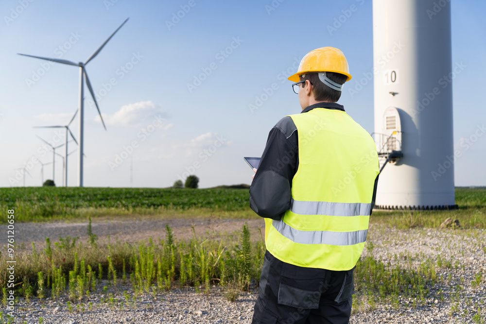 Engineer with digital tablet works on a field of wind turbines