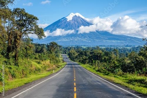 A scenic road leading towards a majestic snow-capped volcano, surrounded by lush greenery and clear blue skies.