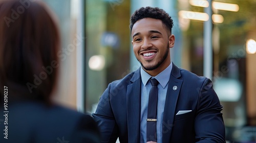 A male employee in a suit smiling warmly while talking to a customer in a professional setting, conveying a friendly and approachable atmosphere.