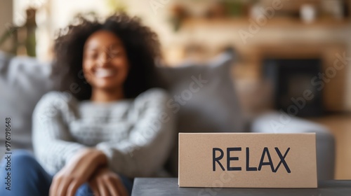 A woman sitting comfortably on a couch with a sign reading 'RELAX' in the foreground, emphasizing the concept of relaxation and leisure at home.
