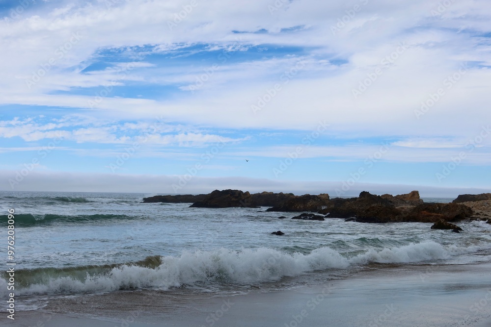 Strong waves rolling onto the beach, with scattered rocks in the water adding texture to the scene. Strong waves rolling onto the beach, with scattered rocks in the water adding texture to the scene.