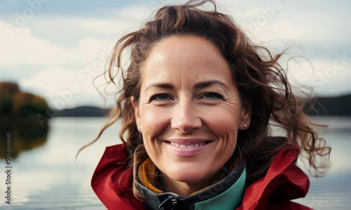 Portrait of smiling woman in raincoat looking at camera on lake shore photo