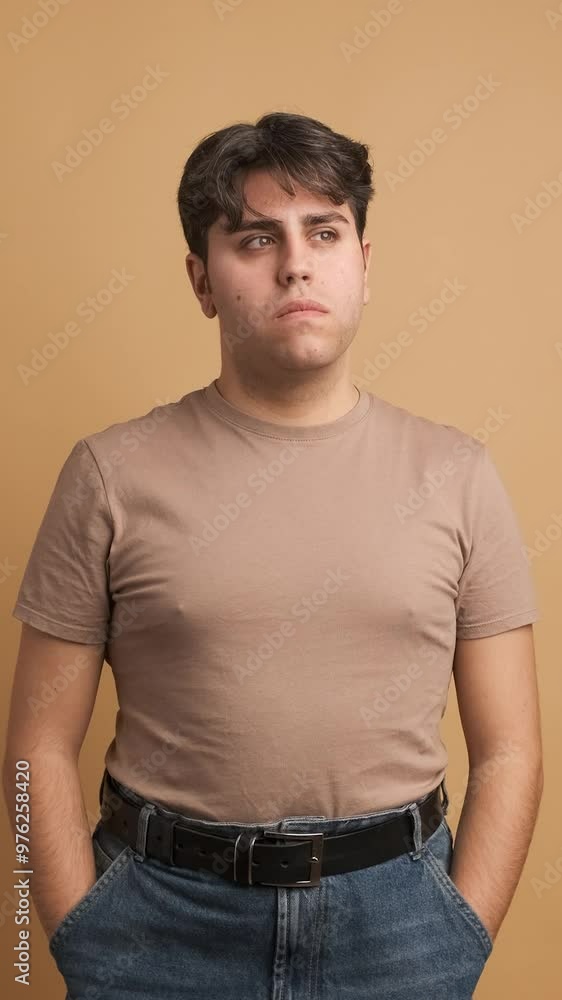 Serious young man looking at camera standing hands on pocket Serious young man looking at camera standing hands on pocket