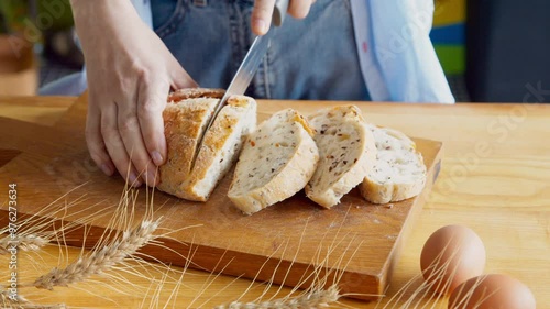 Woman slicing wholegrain bread with seeds on wooden cutting board at kitchen, close up