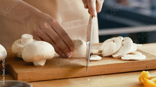 Female hands slicing champignon mushrooms with kitchen knife on wooden cutting board, closeup