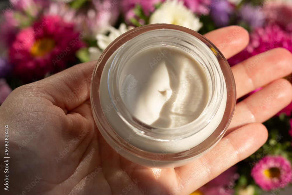 Closeup of a jar of moisturizer surrounded by flowers. Concept of spring skincare.