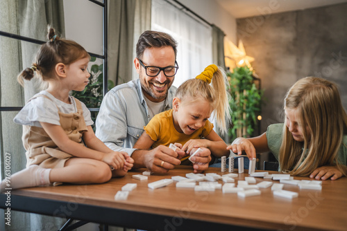 Single father play dominoes with his three young daughters at home