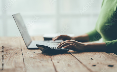 Close-up of a Woman's Hands Using a Calculator and Laptop: A woman's hands are shown in a close-up shot, deftly navigating a calculator and laptop, highlighting the focus and precision of modern busin photo