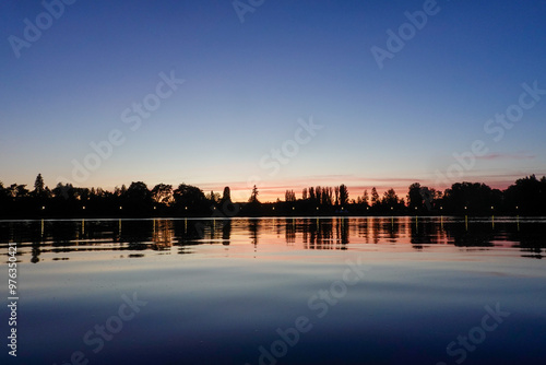 Sunset on the lake with trees in silhouette and blue red sky.