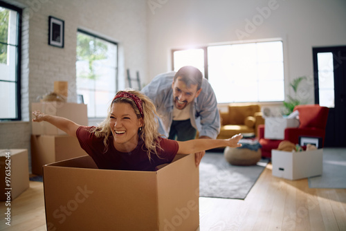 Cheerful woman having fun while being pushed by her husband in cardboard box in their new house.