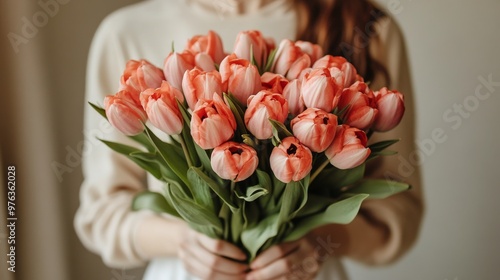 A person holding a beautiful bouquet of pink tulips indoors in soft lighting