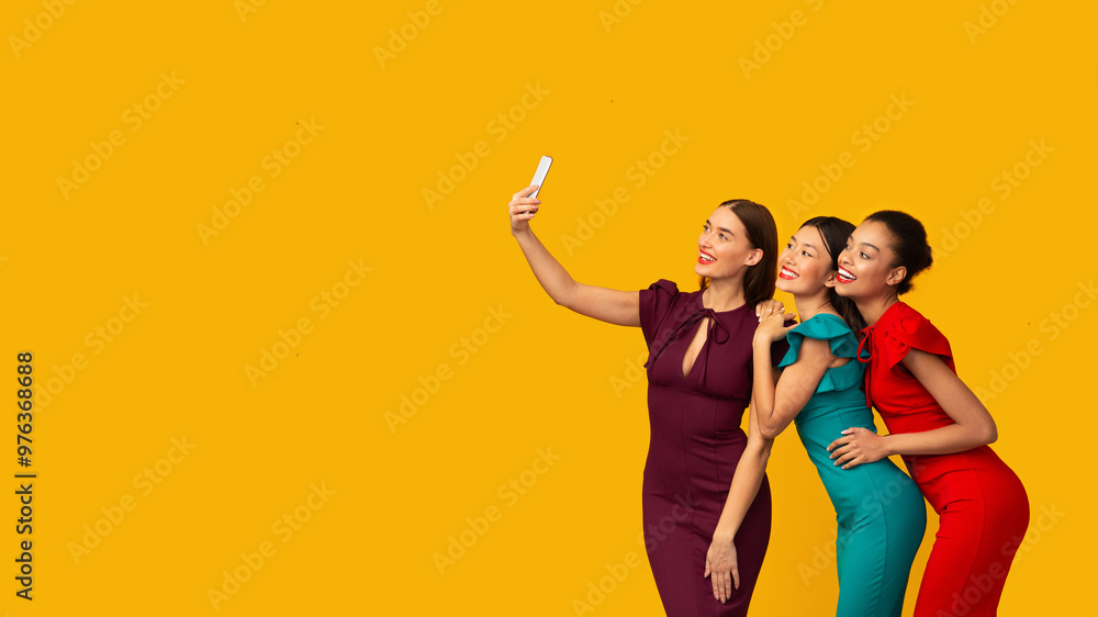 Three Happy Girls In Fancy Dresses Making Selfie Using Smartphone Having Fun On A Party Over Yellow Background. Panorama Three Happy Girls In Fancy Dresses Making Selfie Using Smartphone Having Fun On A Party Over Yellow Background. Panorama