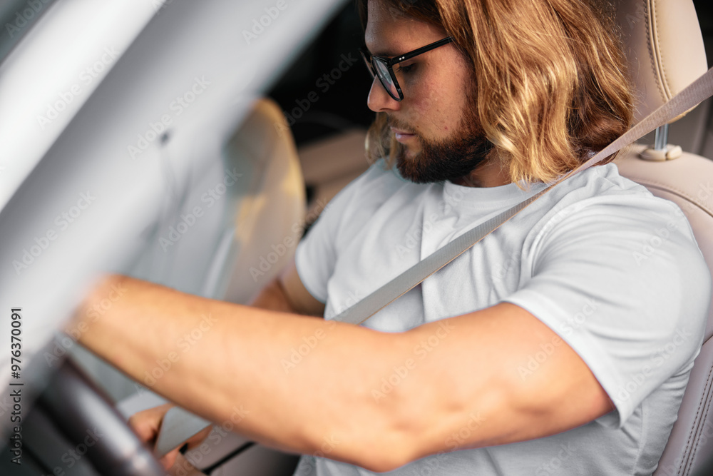 Man with long hair sitting in a car, focused on driving, wearing a white t shirt and sunglasses, modern interior Man with long hair sitting in a car, focused on driving, wearing a white t shirt and sunglasses, modern interior