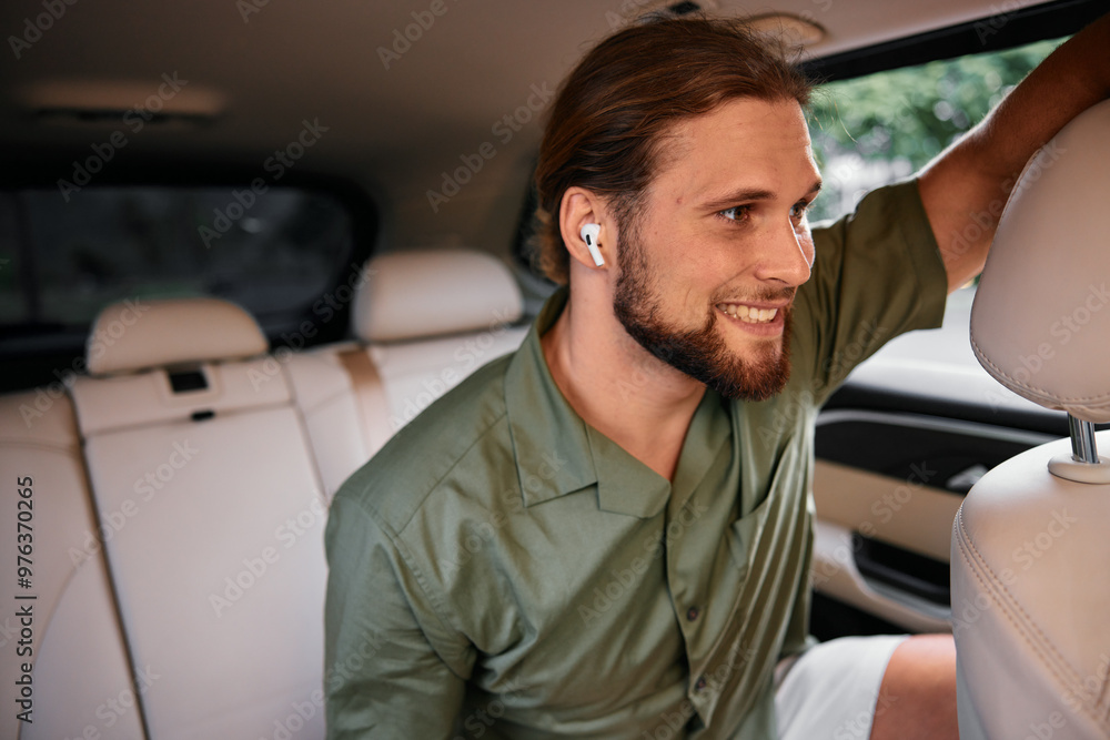 A young man smiling while wearing wireless earbuds in a car s back seat A young man smiling while wearing wireless earbuds in a car s back seat