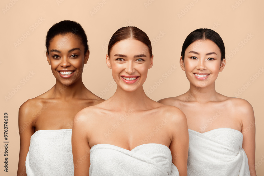 Three Happy Diverse Girls Wrapped In White Towels Posing Standing On Gray Studio Background, Smiling To Camera. Body Care Concept Three Happy Diverse Girls Wrapped In White Towels Posing Standing On Gray Studio Background, Smiling To Camera. Body Care Concept