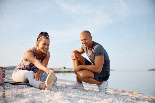 Young athletic couple warming up while exercising on beach. photo