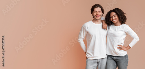 Portrait of happy interracial couple hugging and posing to camera, standing over yellow background with free space