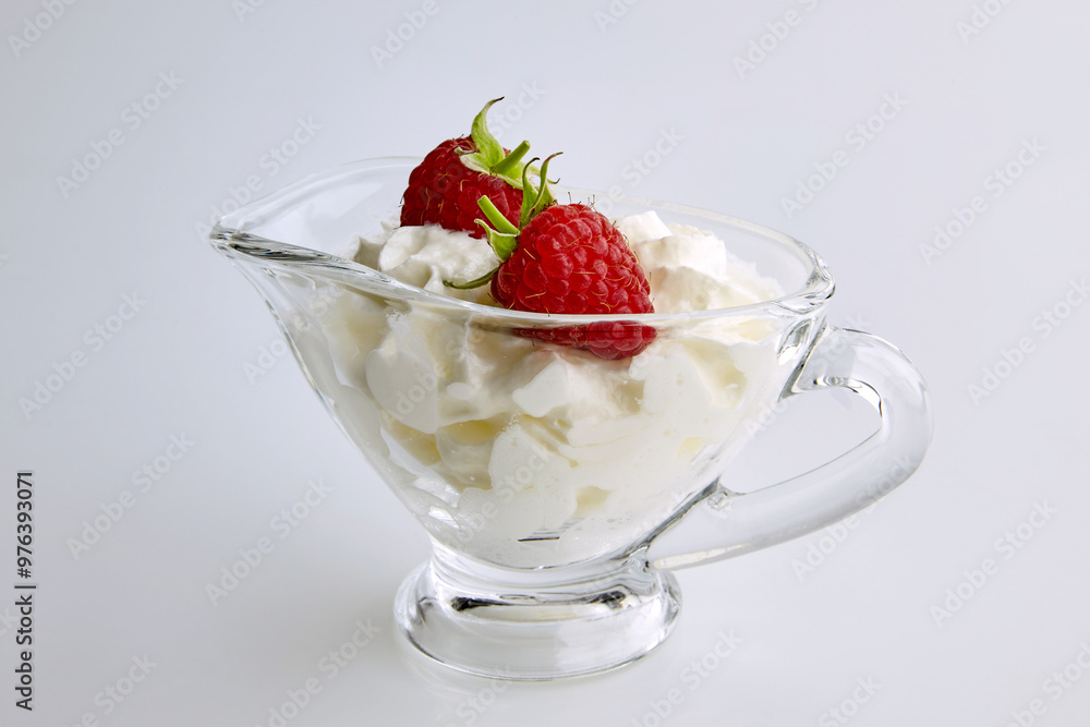 two raspberries and whipped cream in a clear glass sauceboat on a white table two raspberries and whipped cream in a clear glass sauceboat on a white table