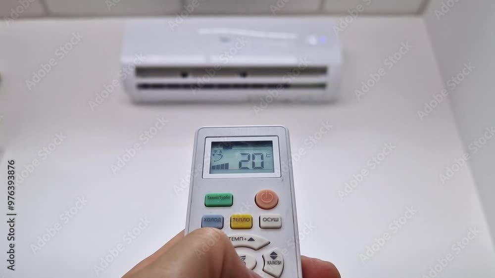 Closeup man hand holding a remote control to the air conditioning system pressing low button trying to adjust the temperature in the room to a comfortable level. Home cooling during heat season Closeup man hand holding a remote control to the air conditioning system pressing low button trying to adjust the temperature in the room to a comfortable level. Home cooling during heat season