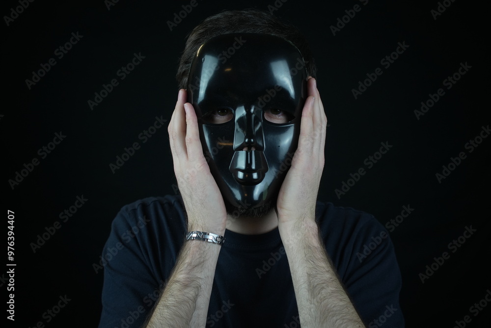 Criminal man covering his face using black theater mask. Black background. Criminal man covering his face using black theater mask. Black background.