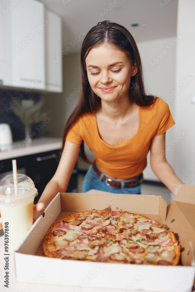 Happy woman in orange shirt holding a box of pizza and a drink in it Happy woman in orange shirt holding a box of pizza and a drink in it