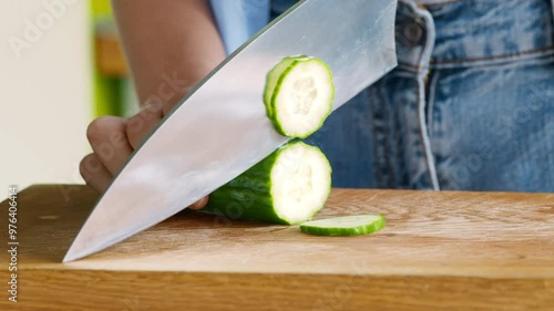 Close up of woman slicing fresh cucumber on cutting board at kitchen
