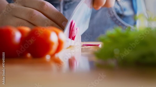 Close up of woman hands with knife cutting radishes on wooden board