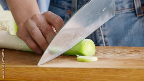 Female hand cutting fresh leek on kitchen board, close up