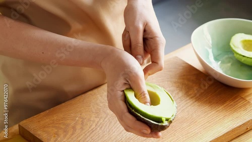 Woman removing avocado half with spoon, and put it into bowl. Healthy vegetarian food