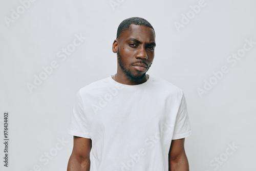 Young African male model in a plain white t shirt, expressing a serious demeanor against a simple light background His confident look and neutral attire create a striking image