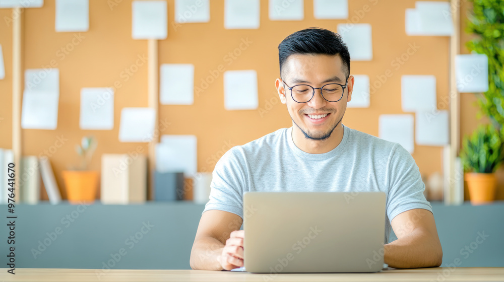 Smiling young man working online on laptop in modern workspace.. Smiling young man working online on laptop in modern workspace..