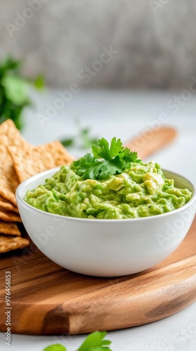 Delicious creamy guacamole served in a bowl with fresh cilantro on a wooden board alongside crispy crackers.