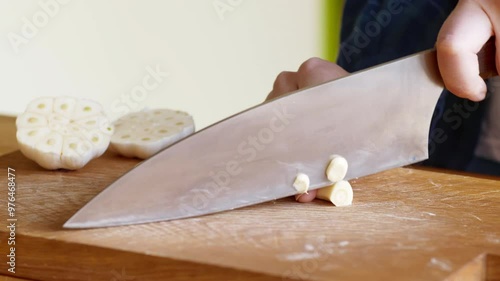 Woman chopping garlic clove on wooden cutting board, close up