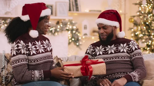 Christmas gifts exchange. Happy african american woman congratulating her boyfriend, giving him present box, Xmas celebration together at home photo