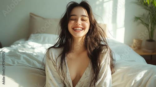 Joyful woman smiling effortlessly in a cozy bedroom, radiating warmth and comfort under soft sunlight.