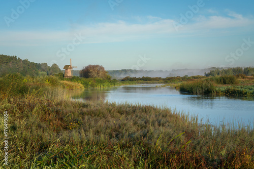 View of an ancient wooden windmill on the banks of the Sorot River on a foggy summer morning, Mikhailovskoye, Pushkinskiye Gory, Pskov region, Russia photo